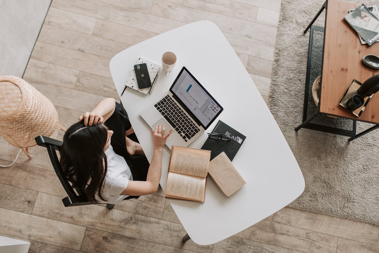 Woman studying at a desk on top of which is her laptop and books